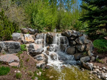 Small waterfall flowing through a park with flowers and trees all aroundの写真素材