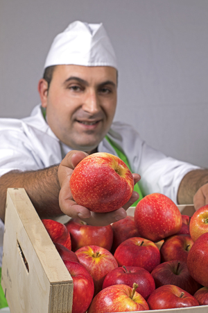 Fruit seller offering a red apple from a box.の写真素材