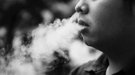 a young asian man smoking  a cigarette in bokeh backgroundの写真素材