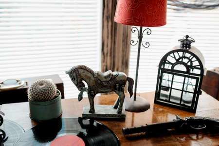 Closeup of metal horse toy, old candle holder, retro red lamp and antique pistol on table.