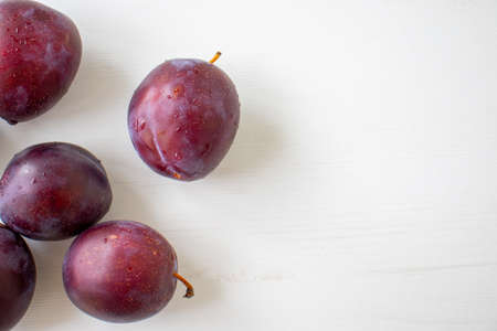 Fresh plums on white wooden background.