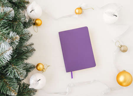 Top view of purple copybook inside frame made of christmas decoration on white wooden background.