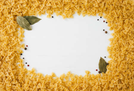 Frame made of macaroni with some bay leaf and peppercorns on white wooden backgroundの写真素材