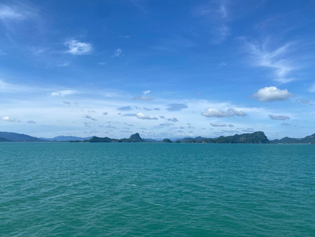 Wide seascape featuring emerald water and distant mountainous islands beneath expansive blue sky...