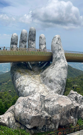 Close-up of colossal stone hand structure appearing to hold elevated pedestrian bridge above lush...