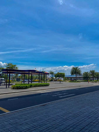 Modern airport roadway with covered passenger pickup area surrounded by tropical palm trees.