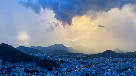 Evening city lights of Nha Trang under dramatic sunset sky with heavy clouds and sun rays.