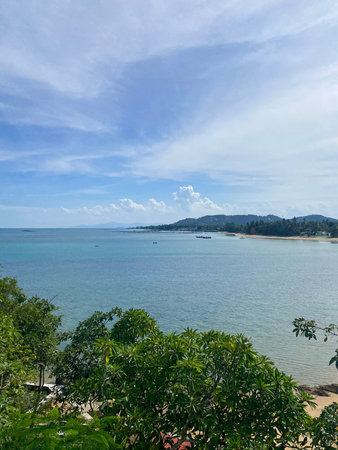 A sweeping panoramic view of Thailand's tropical coastline, with clear blue water, a calm sea, and...