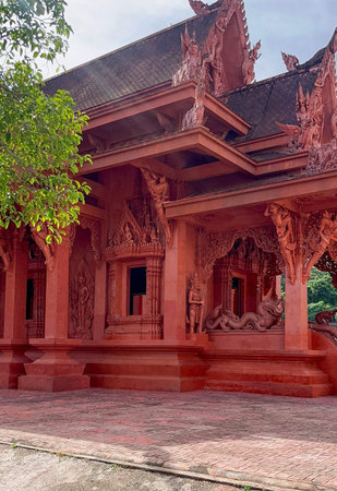 A richly decorated red Thai temple featuring elaborate carvings, mythological guardian sculptures...