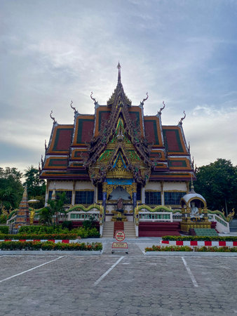 Ornate Buddhist temple building with traditional Thai architecture and decorative roof under cloudy...