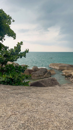 Massive smooth granite rocks near the sea surrounded by tropical vegetation. The ocean horizon and dramatic cloud formations create a scenic coastal environment in Thailand.の写真素材