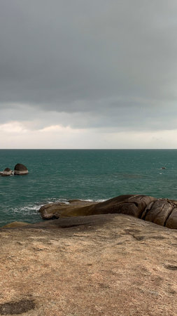 Dramatic storm clouds hanging over a turquoise tropical sea with large granite rocks along the...