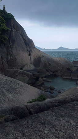 Rock formations and a small sandy bay along a tropical coastline. People exploring the rocks add...