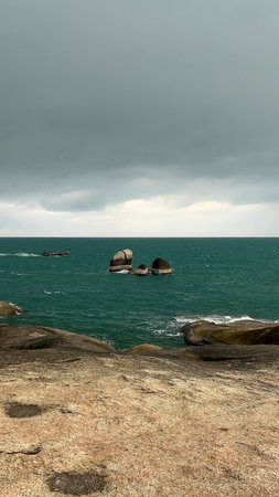A traditional longtail boat sailing near large rock formations in turquoise tropical ocean water under dramatic clouds.の写真素材