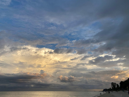 Wide tropical beach with dramatic sunset clouds and calm ocean water.