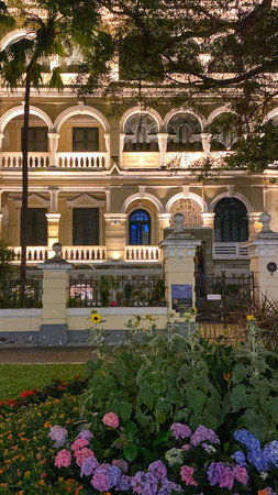 Elegant historic mansion with classical arches and balconies illuminated at night surrounded by colorful flower garden.の写真素材