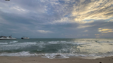 Seascape with waves breaking on sandy tropical beach under textured cloudy sky at sunset.