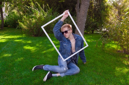 Young human on the green grass, he is wear jeans jacket, jeans and white scarf, he has white frame and blue goggles. He has take a restの写真素材