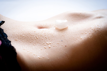 Wet female flat tummy with a slice of ice in the form of heart