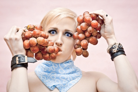 the young guy the gay sensually eats grapes which holds near the person on a pink backgroundの写真素材