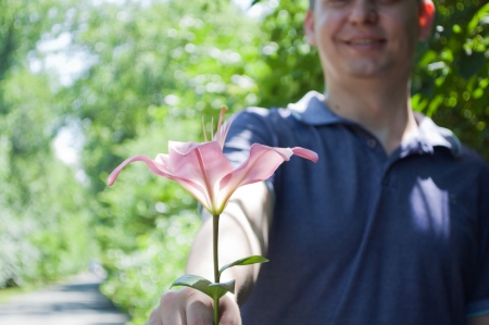 the young man outdoors gives the pink lilyの写真素材