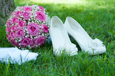 white shoes, pink bouquet from roses and a beautiful handbag of the bride on a green grassの写真素材