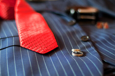 wedding rings, red tie, belt and cuff links lie on a wedding suit of the groomの写真素材