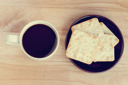 Cup of coffee on wooden table with cracker in plateの写真素材