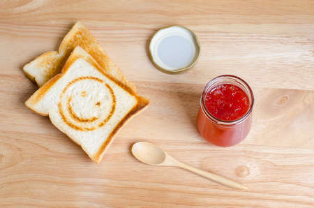 Strawberry jam and toasted bread with smiling burn mark on wooden tableの写真素材