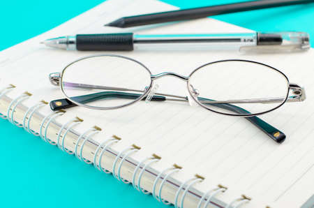 Old glasses with pen and pencil on open notebookの写真素材