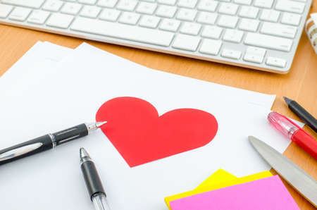 Red heart on white paper with pen on computer deskの写真素材