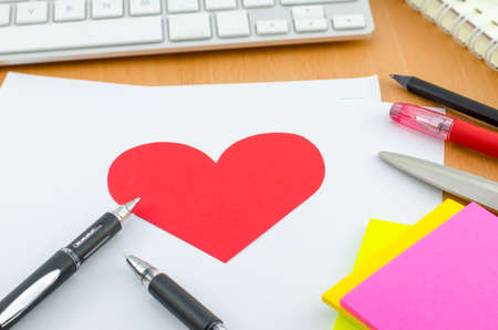 Red heart on white paper with pen on computer deskの写真素材