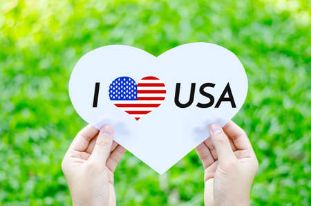 Hand holding white heart paper with I love USA text on blur green grass background  independence day