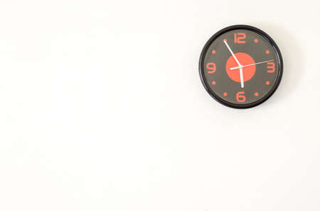 Black modern wall clock on white concrete wall with palce for text