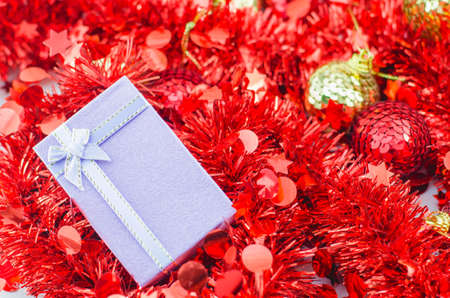 Christmas background - Purple gift box with ribbon bow on red tinsel and xmas ballsの写真素材