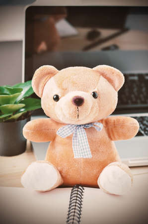 Brown teddy bear with blue ribbon bow place on computer desk - Vintage and vignette toneの写真素材