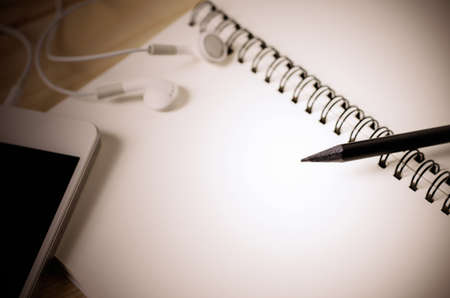 Close up of black pencil and blank white sketchbook on wooden table with vintage and vignette toneの写真素材