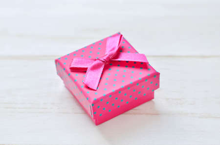 Pink gift box with dot pattern and ribbon bow on white wooden tableの写真素材