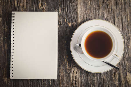 White notebook and cup of black tea on wooden table with vintage and vignette colorの写真素材