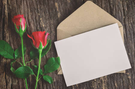 Blank white greeting card with brown envelope and red rose flowers on wooden table with vintage and vignette tone - Valentine and love conceptの写真素材