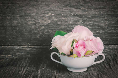 Artificial rose in white cup on old wooden table with vintage and vignette tone