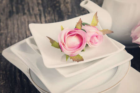 Artificial rose in white plate on old wooden table with vintage and vignette tone