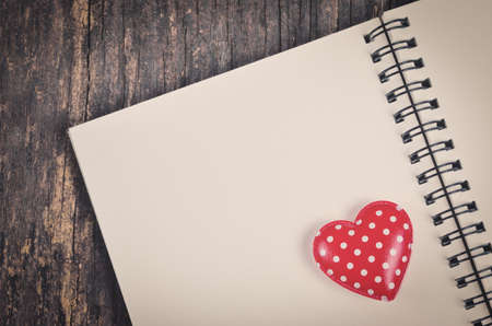 Red retro heart and white notebook on old wooden table with vintage and vignette toneの写真素材