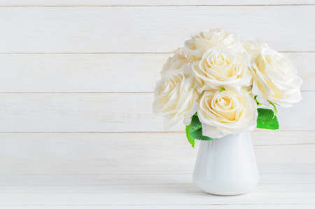 White artificial roses in vase on old white vintage wooden backgroundの写真素材