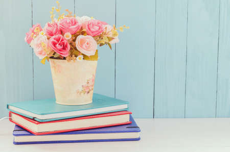 Pastel Artificial Pink Rose Bouquet in flower pot with pile of notebooks on white and blue wooden...