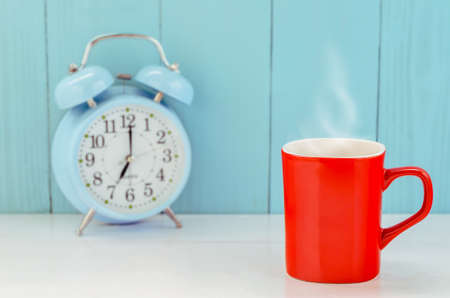 Red coffee mug with hot steam and blue vintage alarm clock on white and blue backgroundの写真素材