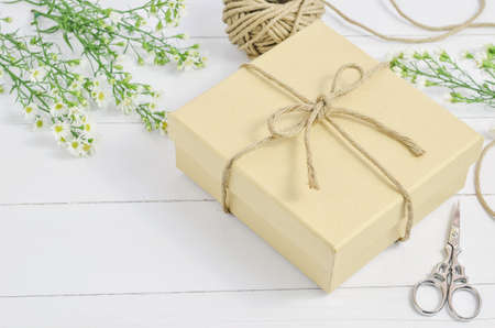 Brown gift box with recycle ribbon bow on wooden background with white daisy flower and vintage toneの写真素材