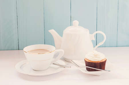 Tea time, Vanilla cupcake with cup of milk tea and white teapot on blue and white wooden background with soft vintage toneの写真素材