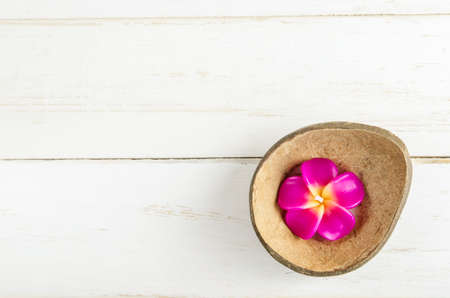 Pink Plumeria aromatherapy candle in brown coconut shell on white wooden background