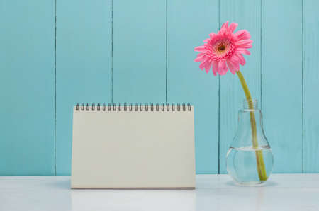 Blank desk calender with pink Gerbera daisy flower in bulb glass vase on white and wooden backgroundの写真素材